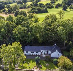 An aerial view of a white house with a garden surrounded by trees and a grassy landscape at Ty Bach - Beaumaris in Beaumaris
