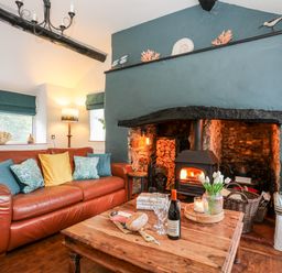 A living room with a leather sofa cushions a wooden coffee table a wood-burning stove and a window seat at Ty Bach - Beaumaris in Beaumaris
