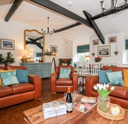 A living room with leather sofas cushions a wooden coffee table and dining area at Ty Bach Beaumaris