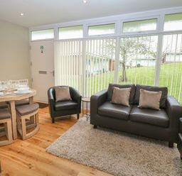 A living room with leather sofa and chairs beside a dining table with tableware at 107 Kings Chalet Park in Cromer