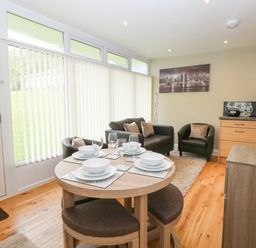 A small dining table set for four next to a seating area with two armchairs and a sofa at 107 Kings Chalet Park in Cromer