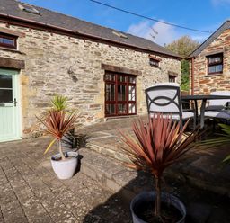 An outdoor patio area with potted plants stone walls two stone buildings a table with four chairs and a green door at Great Meadow Barn in Crantock