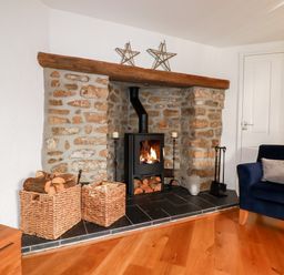 A stone fireplace with a wood-burning stove and baskets of firewood in a living room at Great Meadow Barn in Crantock