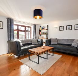 A living room with two black leather sofas a wooden coffee table a bookshelf and framed pictures at Great Meadow Barn in Crantock