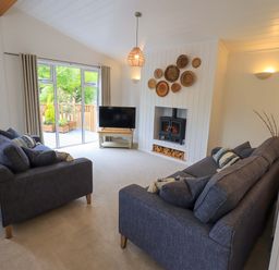 A living room with two blue sofas a wood burning stove and a television at Hollytree Lodge Beckside 1 Limefitt Park near Windermere