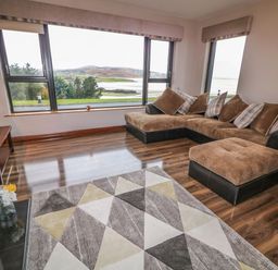 A living room with a brown sectional sofa a geometric patterned rug and large windows overlooking a landscape at Upper Killult in Killult near Gortahork County Donegal