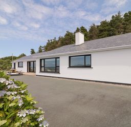 An exterior view of a white house with black window frames and a grey roof surrounded by trees and flowers at Upper Killult in Killult near Gortahork County Donegal