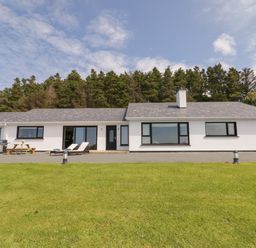 A single story white house with large windows and outdoor seating on a lawn surrounded by trees at Upper Killult in Killult near Gortahork County Donegal