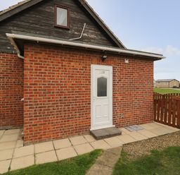 A brick building with a white door numbered 235 and a small fenced garden area at Chalet 235 in Wilsthorpe near Bridlington