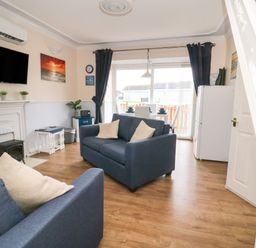 A living room with blue sofas a mounted television and a dining table near patio doors at Chalet 235 in Wilsthorpe near Bridlington