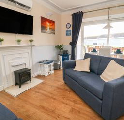 A living room with two blue sofas a TV above a fireplace and a dining table near a sliding glass door at Chalet 235 in Wilsthorpe near Bridlington