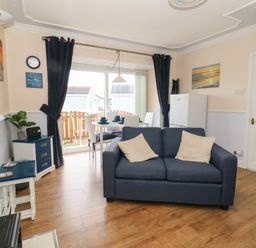 A living room with a blue sofa white dining table and chairs a small fridge and a television at Chalet 235 in Wilsthorpe near Bridlington