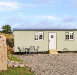 A small light green cabin with two windows and a white door with steps outside and a glass table with four chairs on a gravel area at Shepherds Retreat Glenlark Gortin near Greencastle