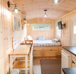 A small wooden cabin interior with a bed a table chairs a wall-mounted television and a kitchen counter at Shepherds Retreat Glenlark Gortin near Greencastle