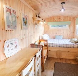 A small wooden room with a bed a table two chairs wall art and a mounted television at Shepherds Retreat Glenlark in Gortin near Greencastle