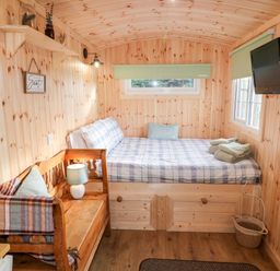 A small wooden room with a bed that has plaid bedding and folded towels a wooden bench with a lamp and pillow a wall-mounted tv and small windows at Shepherds Retreat Glenlark Gortin near Greencastle