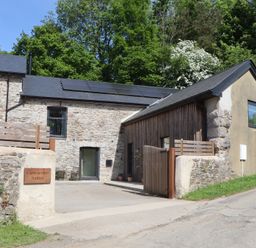 A stone building with solar panels on the roof and a wooden gate at 3 Caddaford Barns in Buckfastleigh