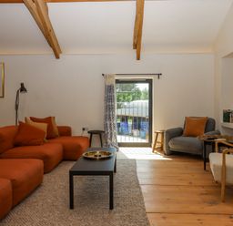 A living room with orange and gray seating wooden beams and a black coffee table at 3 Caddaford Barns in Buckfastleigh