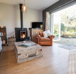 A living room with a wood stove a leather armchair a wooden coffee table and an open door to a garden at The Croft in Newport Pembrokeshire