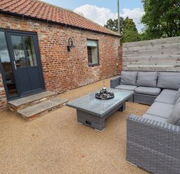 An outdoor patio area with a gray wicker sectional sofa a glass coffee table and a brick building at Partridge Place Burton Pidsea