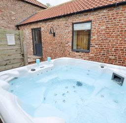 An outdoor hot tub with two blue glasses near a brick house with a black door and window at Partridge Place in Burton Pidsea