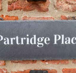 A dark stone sign with white text reading Partridge Place mounted on a red brick wall at Partridge Place Burton Pidsea