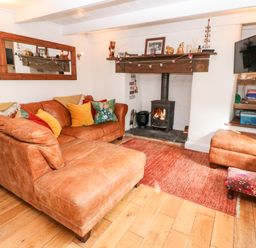 A living room with a leather sectional sofa and a wood burning stove at Honeysuckle Cottage in St Agnes