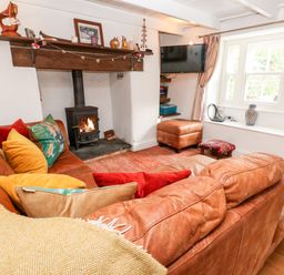 A living room with a brown leather sofa colorful cushions a wood burning stove and a wall mounted television at Honeysuckle Cottage in St Agnes