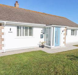 A single story house with a blue door and white walls with windows and a lawn at Palm View in Holywell Bay