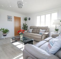 A living room with two sofas a glass coffee table a mounted television and plants at Palm View in Holywell Bay