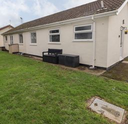The exterior of a single-story cream colored house with a lawn bench and storage box on the side at 13 Gower Holiday Village in Scurlage