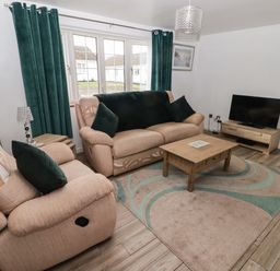 A living room with beige sofas green cushions a coffee table and a television at 13 Gower Holiday Village in Scurlage