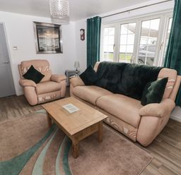 A living room with beige sofas green cushions wooden coffee table and large windows with green curtains at 13 Gower Holiday Village in Scurlage