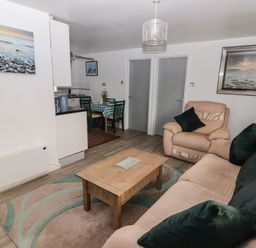 A living room with a sofa and armchair around a wooden coffee table and a dining area with a table and chairs at 13 Gower Holiday Village in Scurlage