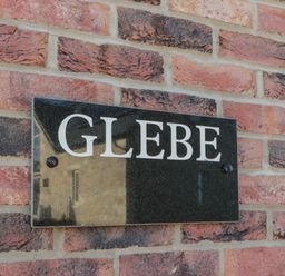 A black rectangular sign with white letters spelling glebe mounted on a brick wall at Glebe Cottage in Embleton