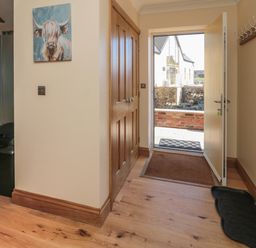 An entryway with an open door leading outside a wooden closet a wall coat rack and a painting of a cow at Glebe Cottage in Embleton