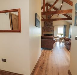 A hallway with a mirror leading to a living room with wooden beams a brick fireplace brown sofas and a dining table at Glebe Cottage in Embleton