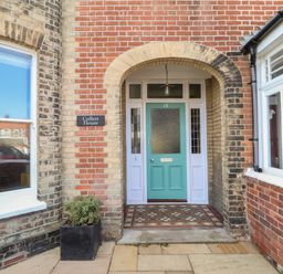 An arched entrance with a turquoise door and tiled floor at Collett House in Southwold