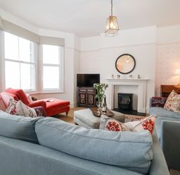A living room with two blue sofas a red armchair a fireplace a television and a window at Collett House in Southwold