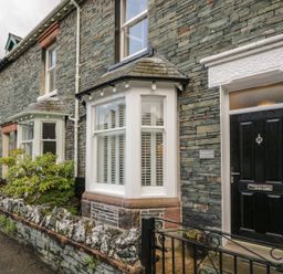 Stone exterior of a house with black front door and white bay window at Derwent Cottage in Keswick