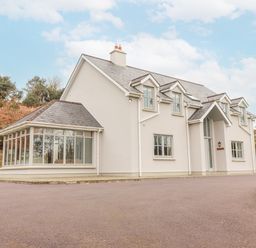 A detached two-story house with multiple windows and a glass extension on a paved driveway at Hazelwood in Leap County Cork