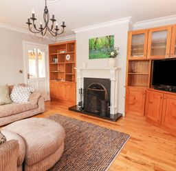 A living room with a fireplace two wooden bookshelves a television beige sofa and an ottoman at Hazelwood in Leap County Cork