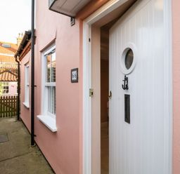 A narrow walkway between two pink houses leading to a wooden gate with house number 64 visible