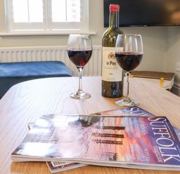 A table with two glasses of red wine a bottle and magazines in a living room at Poppy Cottage in Southwold