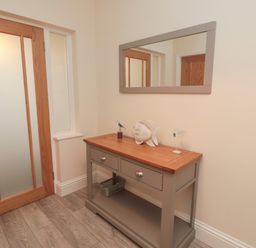 A hallway with a wooden door mirror above a wooden console table with decorative fish and bird figures at Bamburgh Dunes Bamburgh near Seahouses