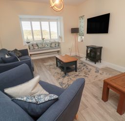 A living room with blue sofas a wooden coffee table a rug and a wall-mounted television at Bamburgh Dunes Bamburgh near Seahouses