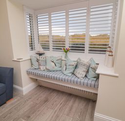 A corner window seat with cushions next to a blue armchair in a room at Bamburgh Dunes Bamburgh near Seahouses
