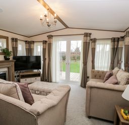 A living room with two beige sofas a television on a stand a fireplace a mirror and glass doors at Hudson's Hideaway in South Lakeland Leisure Village