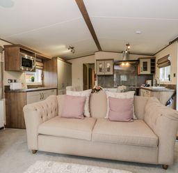 A living room with a beige sofa and pillows facing an open kitchen with cabinets and appliances at Hudsons Hideaway in South Lakeland Leisure Village