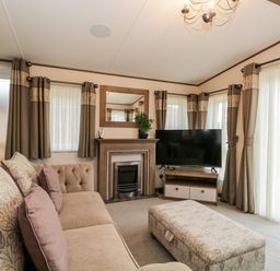 A living room with a sofa ottoman fireplace television and curtains at Hudson's Hideaway in South Lakeland Leisure Village